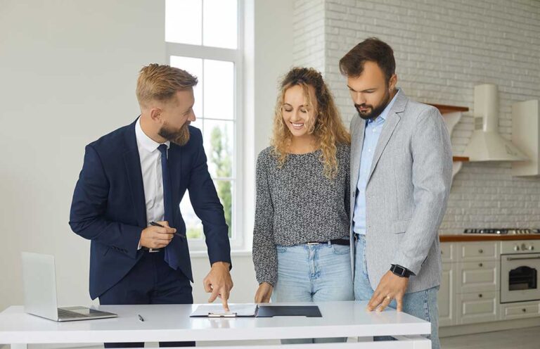 A person sitting at a kitchen table with a folder of documents, discussing with a real estate agent.