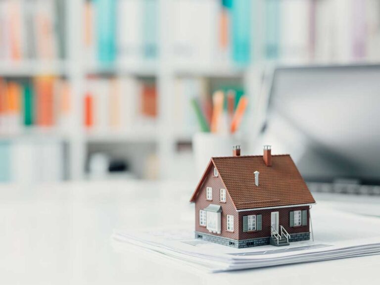 A couple reviews paperwork together at a kitchen table, focusing on financial documents and a laptop.